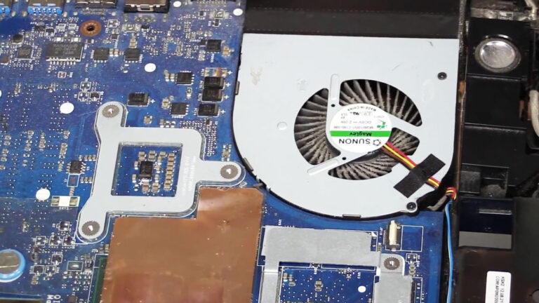 Open laptop showing a CPU cooling fan and motherboard covered with dust and debris during overheating diagnosis.