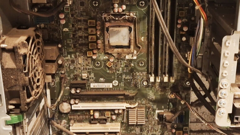 Open desktop computer filled with dust and debris, with the heatsink removed and no usable thermal paste remaining on the processor.