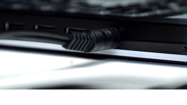 Side of a laptop showing an audio cable connected to the headphone and microphone port during sound troubleshooting.
