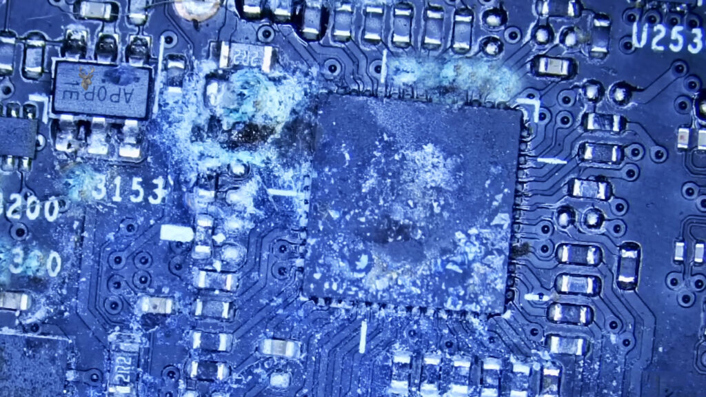 Laptop motherboard with extensive liquid damage and corrosion affecting multiple electronic components.