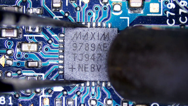 Laptop motherboard with a Maxim 9789AETJ-947 integrated circuit being removed using hot air and precision tweezers during board-level repair.