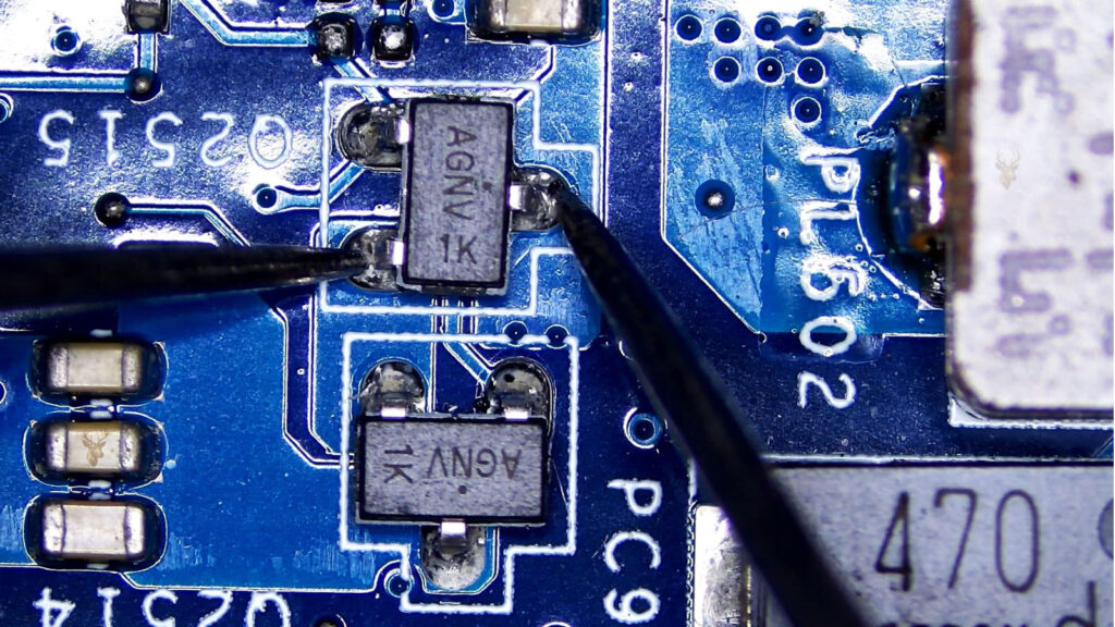 Technician using multimeter probes to test an AGNB transistor on a computer motherboard during electronic diagnostics.
